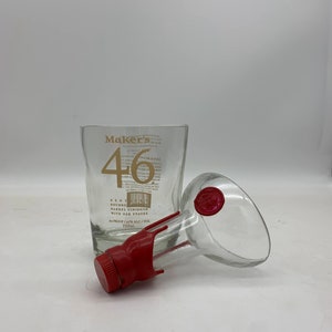 May include: Two empty glass bottles, one with a red plastic cap and the other with a red wax seal. The bottle on the left has the text "Maker's 46" and "Kent Bourbon Barrel Finished with Oak Staves" printed on it. The bottle on the right has a clear glass spout.