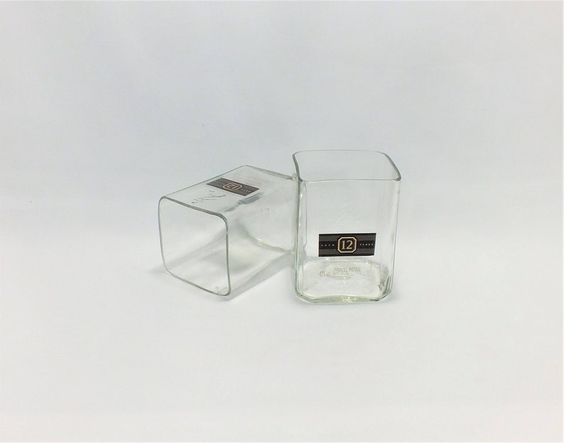 May include: Two clear glass square drinking glasses. The glass on the right has a black label with the number "12" printed on it.