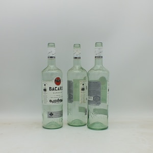 May include: Three clear glass bottles of Bacardi Superior white rum. The bottles are empty and have a textured surface. The labels are white with black text and a red bat logo.