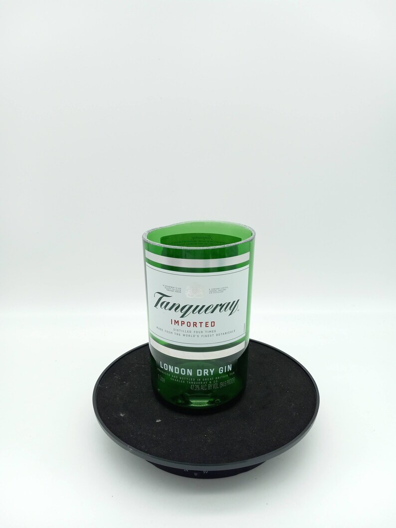 K&ouml;nnte beinhalten: Eine gr&uuml;ne Glasflasche Tanqueray London Dry Gin. Die Flasche steht auf einer schwarzen runden Plattform. Das Etikett lautet "Tanqueray Importiert Viermal Destilliert Aus Den Besten Botanischen Zutaten Der Welt London Dry Gin Hergestellt und Abgef&uuml;llt in Gro&szlig;britannien 1 Liter 47,3% Vol. (94,6 Proof)"
