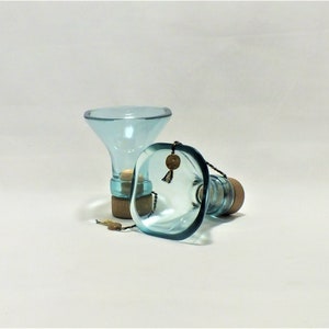 May include: Two clear blue glass bottle stoppers with cork tops. The stoppers are shaped like funnels and have a square base.
