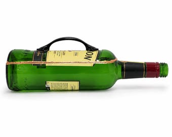 Puede incluir: Una botella de vidrio verde reutilizada con un asa negra y una banda de color cobre. La botella tiene una etiqueta negra y roja y está tumbada horizontalmente sobre una superficie blanca. Es un artículo único.