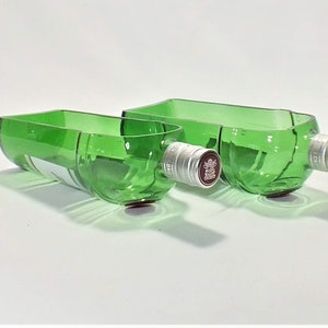 Op de afbeelding: Twee groene glazen kommen gemaakt van gerecyclede wijnflessen. De kommen zijn van verschillende grootte en hebben zilveren flessendoppen.