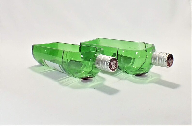 Op de afbeelding: Twee groene glazen kommen gemaakt van gerecyclede wijnflessen. De kommen zijn van verschillende grootte en hebben zilveren flessendoppen.