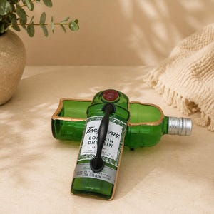 May include: A repurposed green glass bottle with a black handle, featuring the Tanqueray London Dry Gin label. The bottle has been cut and reshaped into a decorative tray with gold trim. A second bottle is visible in the background.