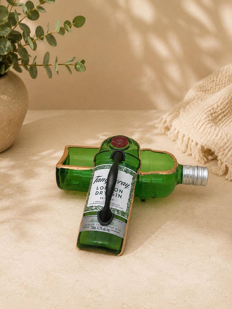 May include: A repurposed green glass bottle with a black handle, featuring the Tanqueray London Dry Gin label. The bottle has been cut and reshaped into a decorative tray with gold trim. A second bottle is visible in the background.