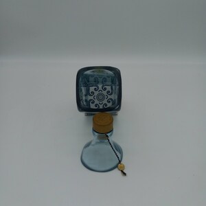 May include: A blue glass bottle with a cork stopper and a blue and white patterned design. The bottle has a string attached to the cork.