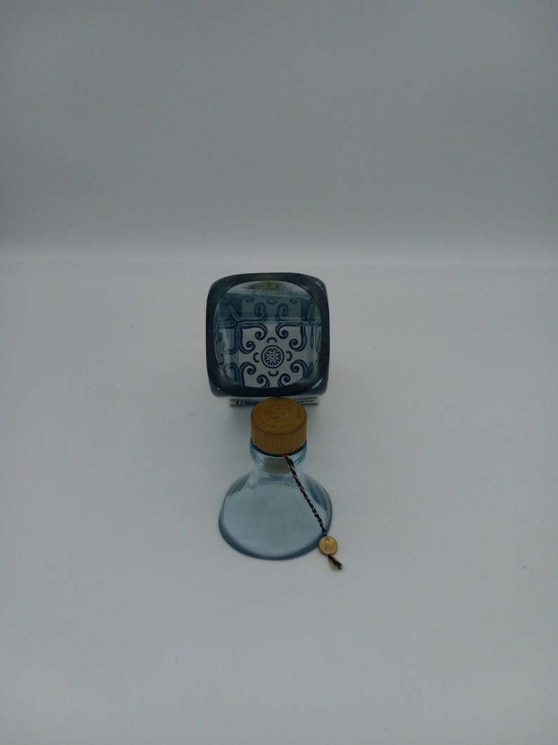 May include: A blue glass bottle with a cork stopper and a blue and white patterned design. The bottle has a string attached to the cork.