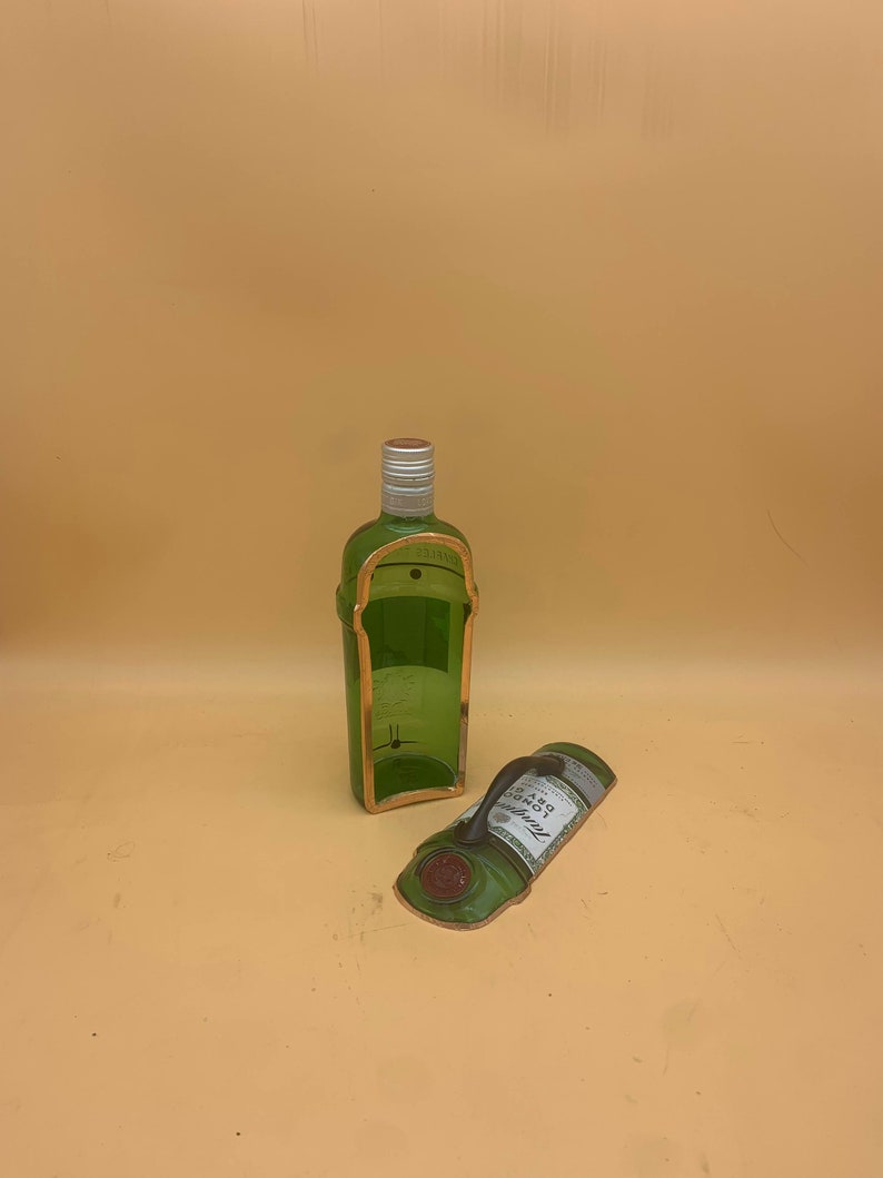 May include: A green glass bottle with a gold-colored trim and a silver cap. The bottle is cut in half, with the label lying next to it. The label reads "Tanqueray London Dry Gin".