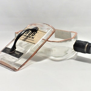 May include: A clear glass bottle with a copper-colored rim and a black handle. The bottle is labeled "Knob Creek" and "100 Proof".