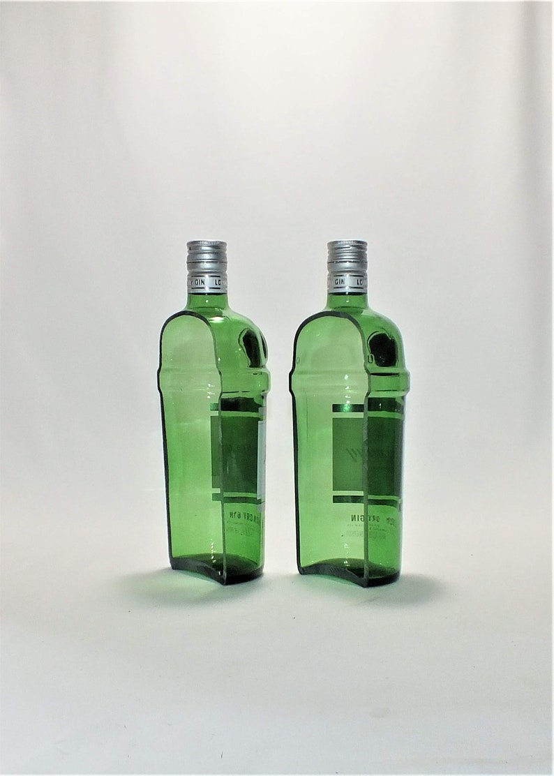 Op de afbeelding: Twee lege groene glazen gin flessen met zilveren doppen. De flessen zijn licht gebogen en hebben een etiket aan de voorkant.