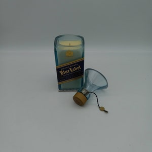 May include: A blue glass candle jar with a white candle inside. The jar is labeled "Johnnie Walker Blue Label Blended Scotch Whisky". The candle is topped with a gold metal lid and a small gold tag.