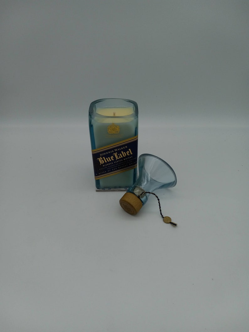 May include: A blue glass candle jar with a white candle inside. The jar is labeled "Johnnie Walker Blue Label Blended Scotch Whisky". The candle is topped with a gold metal lid and a small gold tag.