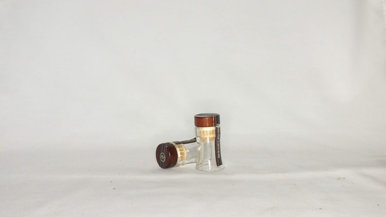 May include: Two clear glass bottles with brown tops and labels. The bottles are sitting on a white surface.