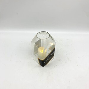 May include: A clear glass candle holder shaped like a bottle with a black label that reads "JOHNNIE WALKER BLACK LABEL" and a white candle inside.