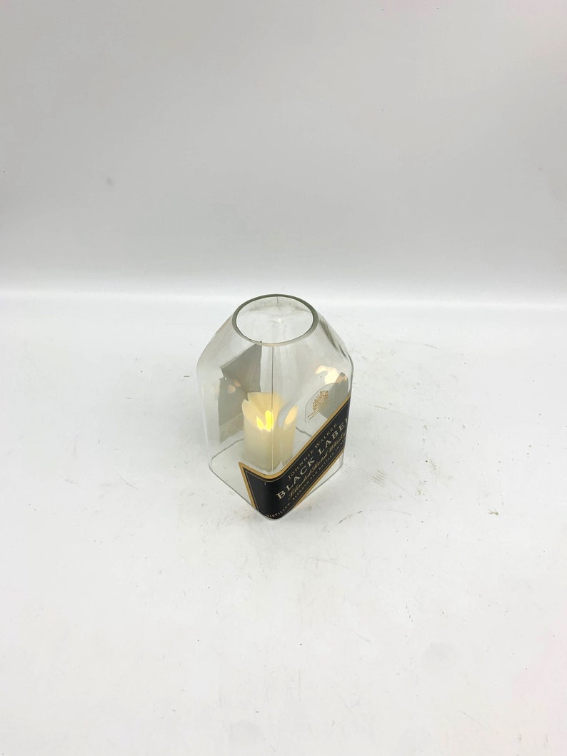 May include: A clear glass candle holder shaped like a bottle with a black label that reads "JOHNNIE WALKER BLACK LABEL" and a white candle inside.