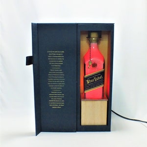 May include: A black box with a red and gold Johnnie Walker Blue Label bottle inside. The bottle is illuminated with a pink light. The box has a description of the whiskey on the side.