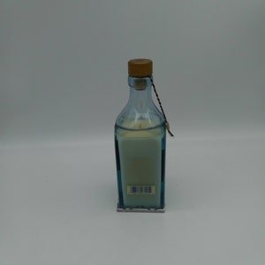 May include: A blue glass candle jar with a wooden lid and a white candle inside. The jar has a blue and white patterned label with a barcode.