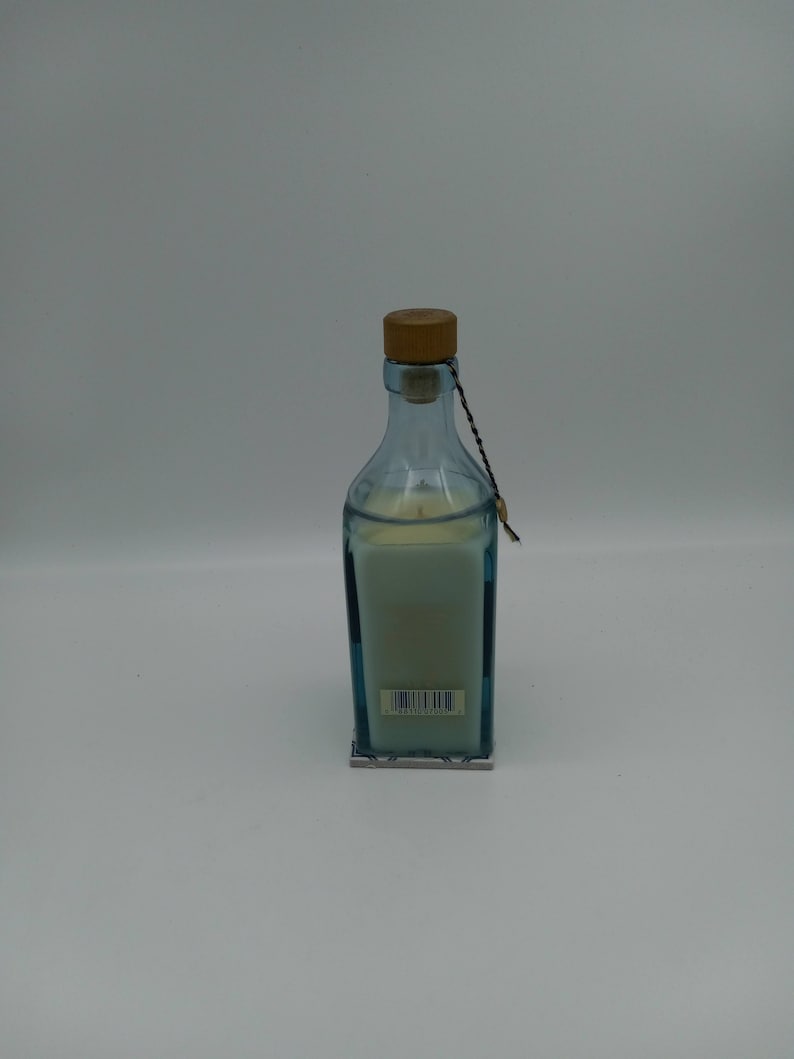 May include: A blue glass candle jar with a wooden lid and a white candle inside. The jar has a blue and white patterned label with a barcode.