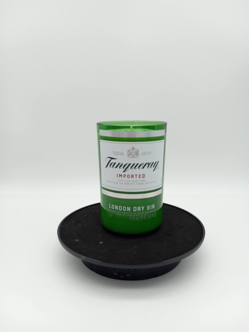 K&ouml;nnte beinhalten: Eine gr&uuml;ne Glaskerze in Form einer Tanqueray London Dry Gin-Flasche. Die Kerze steht auf einem schwarzen Drehteller.