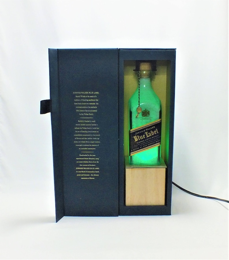 May include: A blue and gold box with a bottle of Johnnie Walker Blue Label Scotch Whisky inside. The bottle is illuminated with a green light. The box has a description of the whisky on the front.