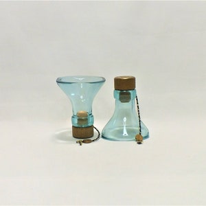 May include: Two glass bottle stoppers with a light blue tint and wooden tops. The stoppers are connected by a thin black and gold string.