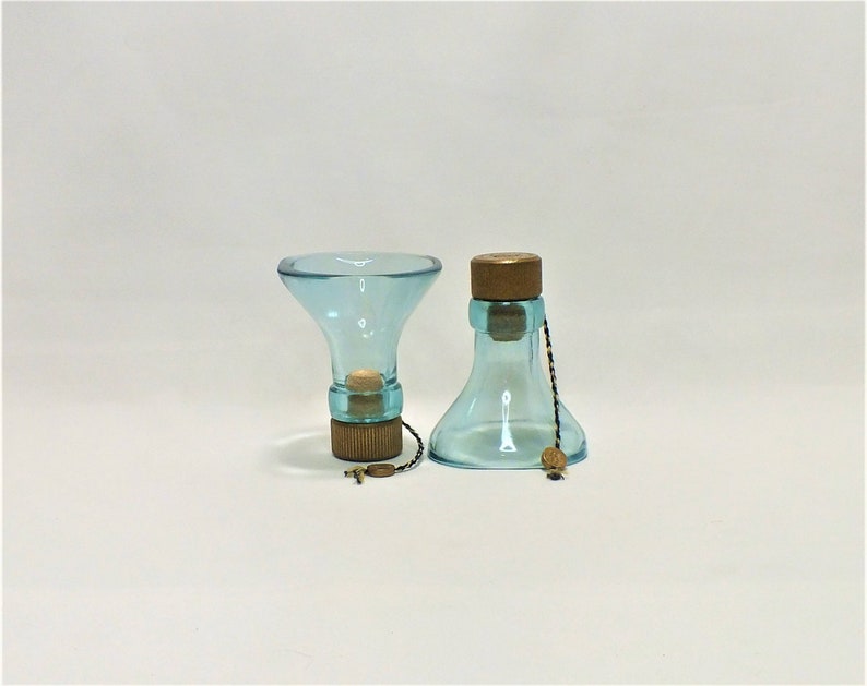 May include: Two glass bottle stoppers with a light blue tint and wooden tops. The stoppers are connected by a thin black and gold string.