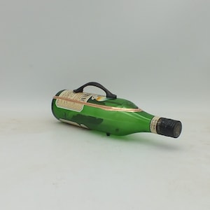 May include: A green glass bottle with a black handle and a gold label. The bottle is lying on its side.