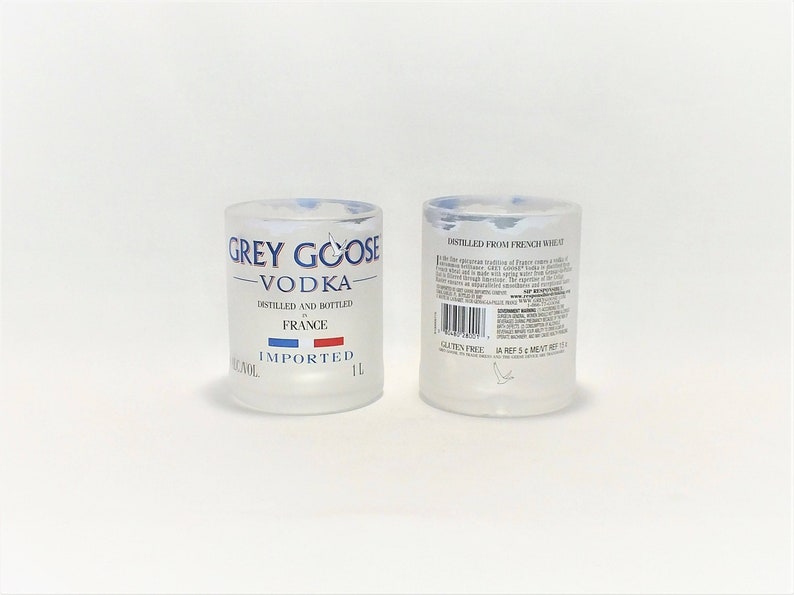 K&ouml;nnte beinhalten: Zwei klare Schnapsgl&auml;ser aus Glas mit mattierter Oberfl&auml;che. Die Vorderseite des Glases zeigt das Grey Goose Vodka-Logo mit dem Text "Grey Goose Vodka", "Destilliert und abgef&uuml;llt in Frankreich" und "Importiert". Die R&uuml;ckseite des Glases zeigt den Text "Destilliert aus franz&ouml;sischem Weizen" und einen Barcode.