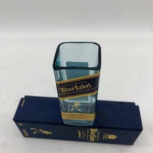 May include: A miniature glass bottle shaped like a Johnnie Walker Blue Label Scotch Whisky bottle. The bottle is clear and has a gold label with the text "Johnnie Walker Blue Label Blended Scotch Whisky" on it.