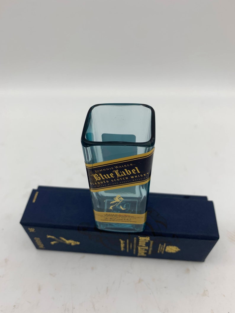May include: A miniature glass bottle shaped like a Johnnie Walker Blue Label Scotch Whisky bottle. The bottle is clear and has a gold label with the text "Johnnie Walker Blue Label Blended Scotch Whisky" on it.