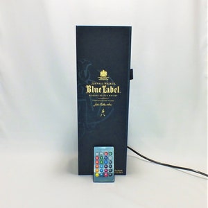 May include: A black box with a gold Johnnie Walker Blue Label Blended Scotch Whisky logo. The box is lit up with a remote control with multiple colored buttons.