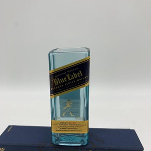 May include: A miniature glass bottle shaped like a Johnnie Walker Blue Label Scotch Whisky bottle. The bottle is clear and has a gold label with the text "Johnnie Walker Blue Label Blended Scotch Whisky" and a walking man logo.