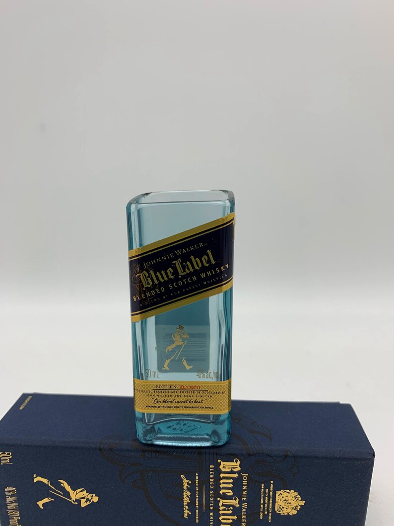May include: A miniature glass bottle shaped like a Johnnie Walker Blue Label Scotch Whisky bottle. The bottle is clear and has a gold label with the text "Johnnie Walker Blue Label Blended Scotch Whisky" and a walking man logo.