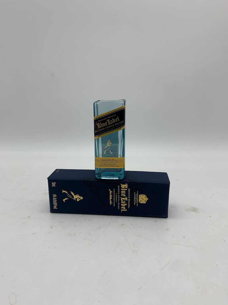 May include: A miniature glass bottle with a blue label that reads "Johnnie Walker Blue Label Blended Scotch Whisky". The bottle is sitting on top of a blue box with the same label.
