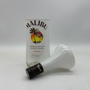 May include: A clear glass bottle of Malibu Caribbean rum with coconut liqueur. The bottle has a white label with the Malibu logo and a palm tree design. The bottle is 1 liter and 21% alcohol by volume. The bottle is sitting on a white surface.