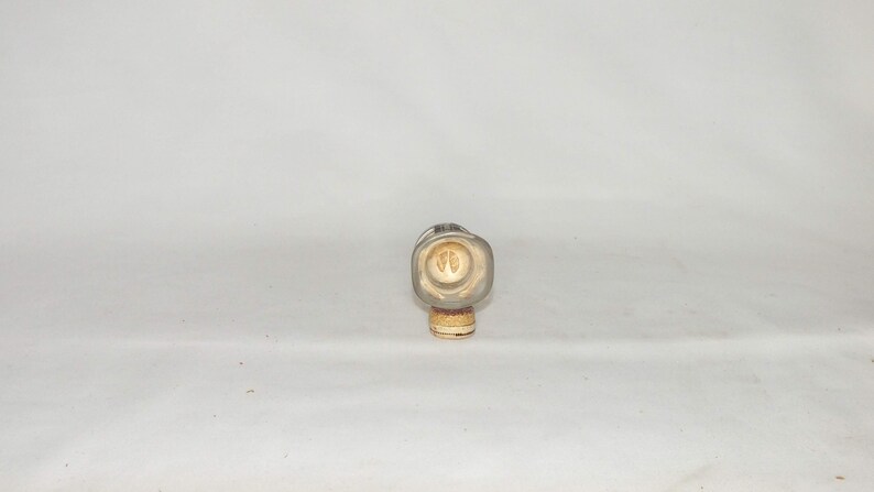 May include: A clear glass bottle with a cork stopper. The bottle has a square shape and a textured surface. The cork stopper has a brown and white design.