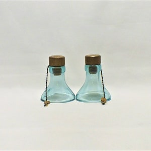 May include: Two clear blue glass bottles with cork stoppers and brown string ties. The bottles have a wide base and a narrow neck.