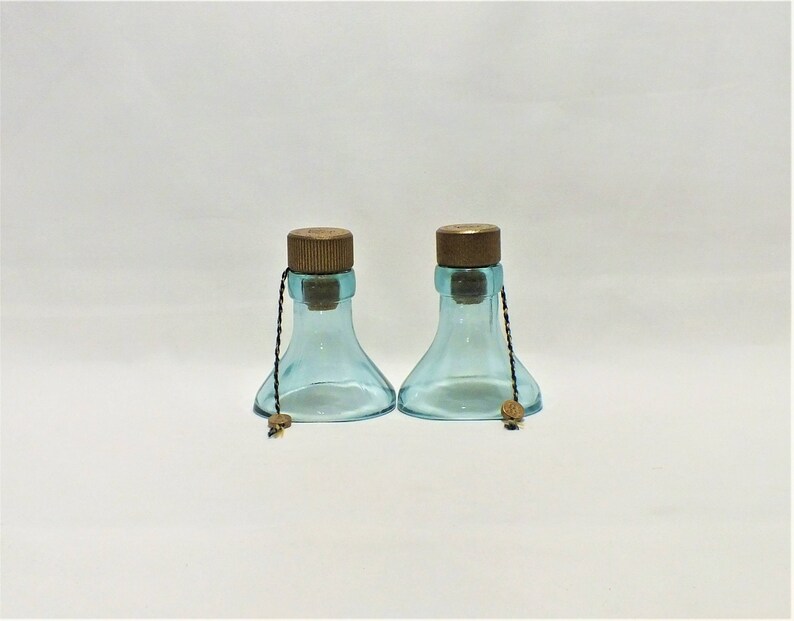 May include: Two clear blue glass bottles with cork stoppers and brown string ties. The bottles have a wide base and a narrow neck.