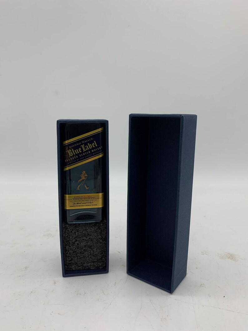 May include: A miniature bottle of Johnnie Walker Blue Label Blended Scotch Whisky in a blue box. The bottle is clear and has a gold label with the Johnnie Walker logo and the words "Blue Label" in gold lettering.