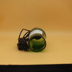 K&ouml;nnte beinhalten: Eine gr&uuml;ne Glasflasche mit einem schwarzen Kabel daran. Die Flasche hat ein Etikett mit der Aufschrift "Gordon's Dry Gin" und liegt auf der Seite.