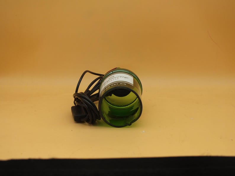 K&ouml;nnte beinhalten: Eine gr&uuml;ne Glasflasche mit einem schwarzen Kabel daran. Die Flasche hat ein Etikett mit der Aufschrift "Gordon's Dry Gin" und liegt auf der Seite.