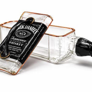 May include: A clear glass whiskey bottle repurposed into a decorative box. The box features a black handle and a label with the text "Jack Daniel's Tennessee Whiskey". The box has a capacity of 750 ml.