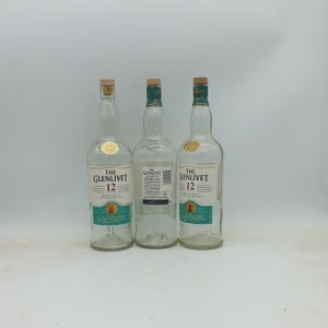 May include: Three clear glass bottles of The Glenlivet 12 year old single malt Scotch whisky. The bottles are all the same size and shape, and they have a green label with the brand name and age printed on them.