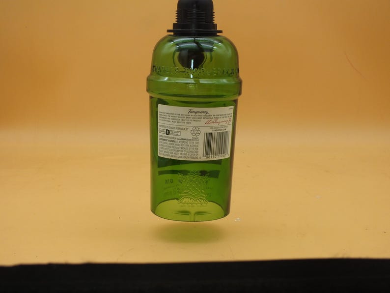 K&ouml;nnte beinhalten: Eine gr&uuml;ne Glasflasche mit schwarzem Verschluss. Die Flasche hat ein Etikett mit dem Text "Tanqueray" und weiteren Informationen zum Produkt. Die Flasche h&auml;ngt am Verschluss.