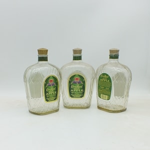 May include: Three clear glass bottles of Crown Royal Regal Apple flavored whisky. The bottles have a textured diamond pattern and a green label with gold lettering.