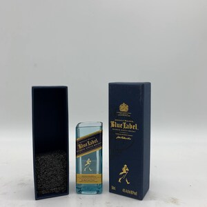 May include: A miniature bottle of Johnnie Walker Blue Label Blended Scotch Whisky in a blue box. The bottle is clear glass with a blue label and the Johnnie Walker logo. The box is blue with gold lettering and a gold crest.