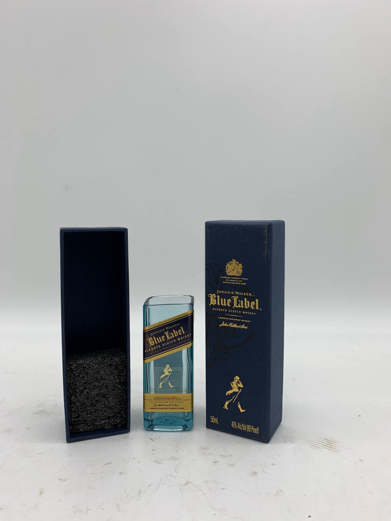 May include: A miniature bottle of Johnnie Walker Blue Label Blended Scotch Whisky in a blue box. The bottle is clear glass with a blue label and the Johnnie Walker logo. The box is blue with gold lettering and a gold crest.