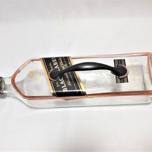 Puede incluir: Una bandeja de servicio hecha de una botella reciclada de Johnnie Walker Black Label. La bandeja de vidrio transparente tiene un borde de color cobre y un asa negra. La etiqueta original a&uacute;n es visible.