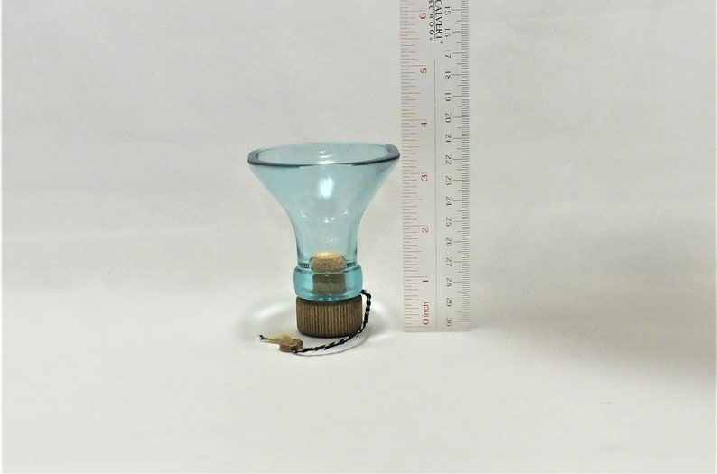 May include: A light blue glass funnel with a cork stopper and a wooden base. The funnel is approximately 10 cm tall.